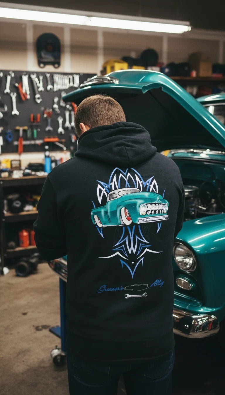 Greaser's Alley Ford Truck pullover hoodie worn in a garage beside a teal custom pickup